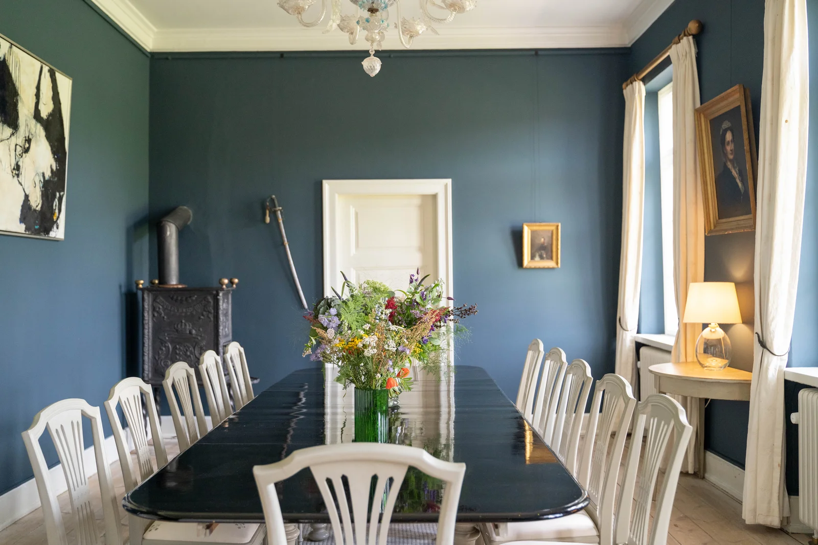 Das Speisezimmer von Gut Agerup mit langer Tafel, weißen Stühlen und gusseisernem Ofen
