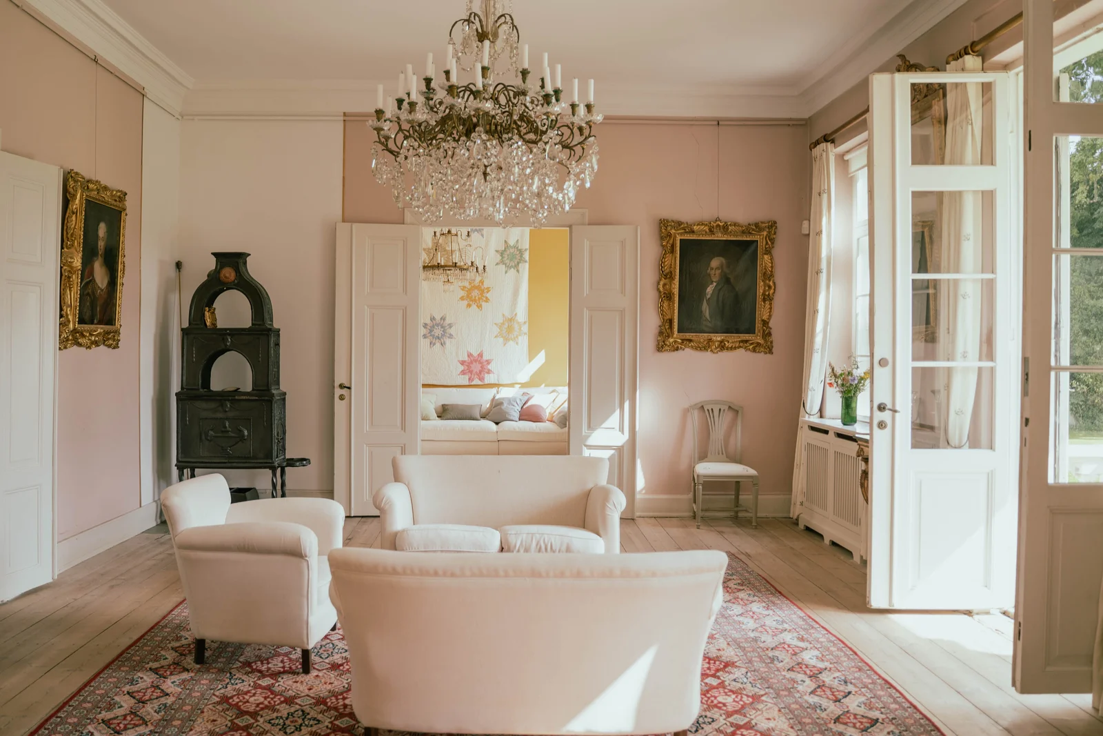 Der Salon von Gut Agerup mit Kristallleuchter, weißen Sofas und Blick ins gelbe Zimmer