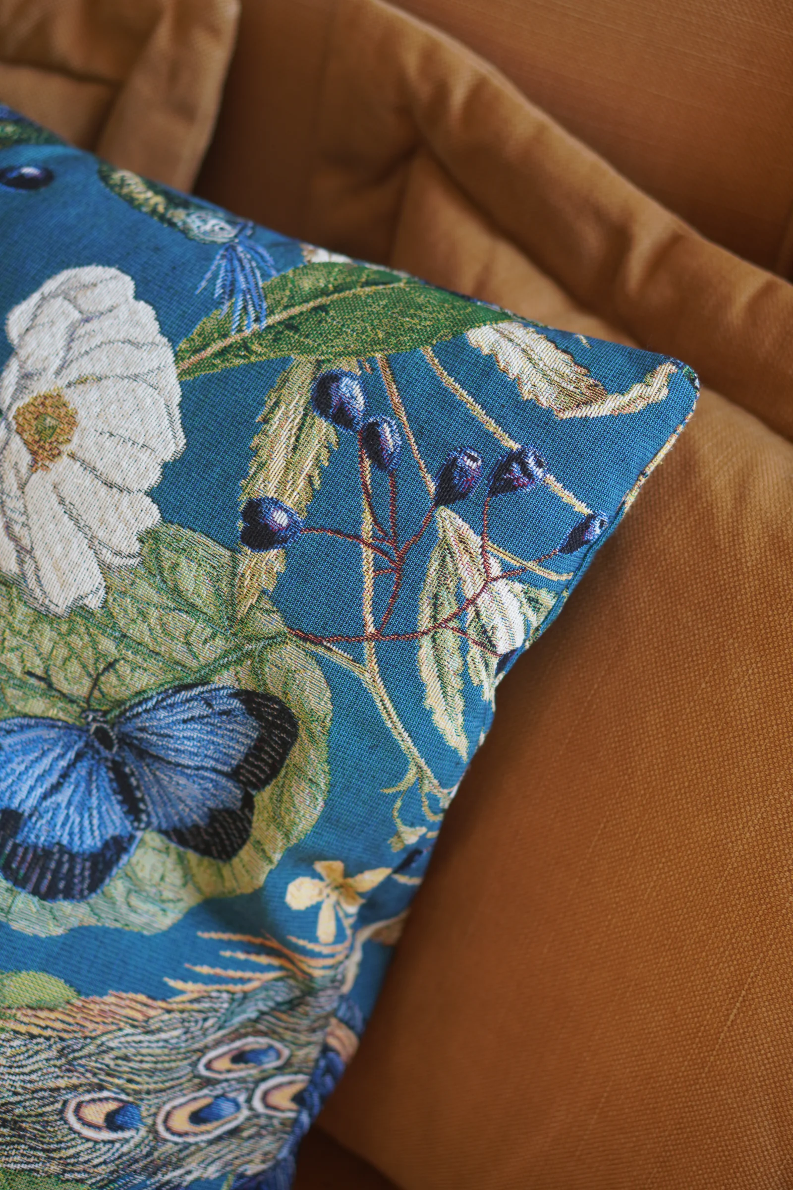 Kissen mit Schmetterlingen und Blumen auf einem ockerfarbenen Sofa im Herrenhaus von Gut Agerup