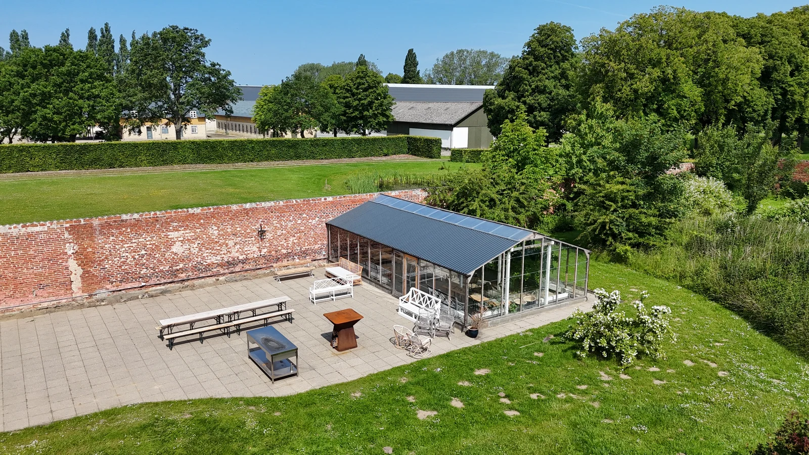 Glashuset og terrassen i den murede have på Agerup Gods med lange borde