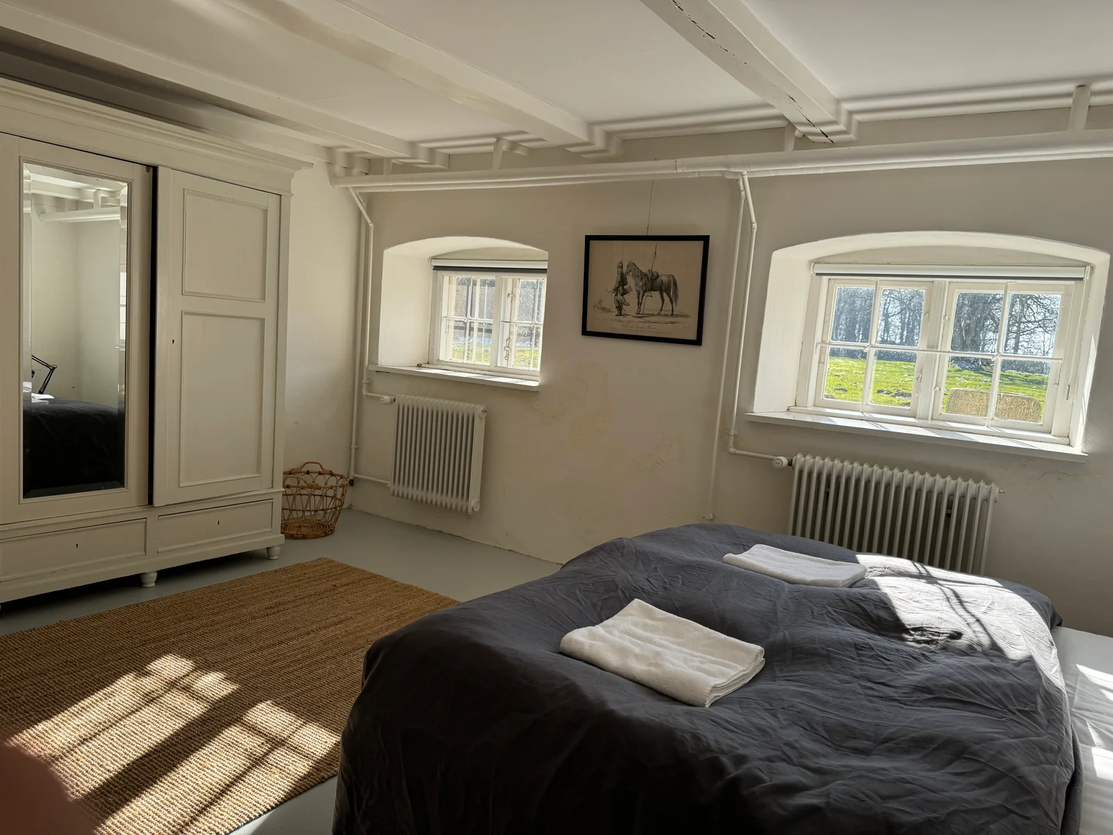 Gästezimmer auf Gut Agerup mit Kleiderschrank, Pferdezeichnung und Sonnenlicht auf dem Bett