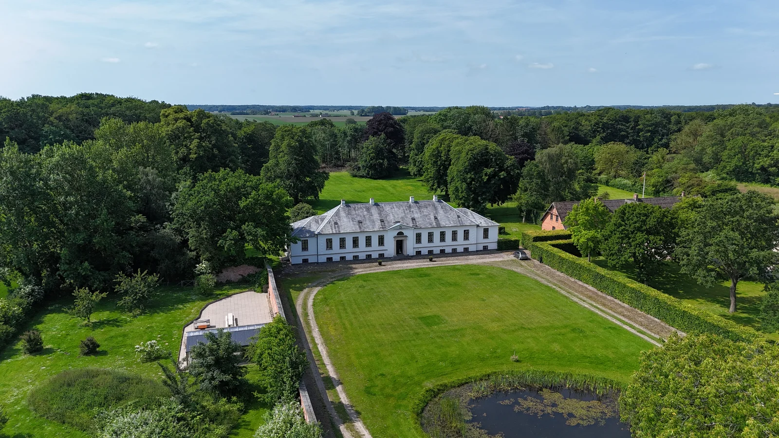 Luftaufnahme des Herrenhauses von Gut Agerup mit Rasen, Teich und ummauertem Garten