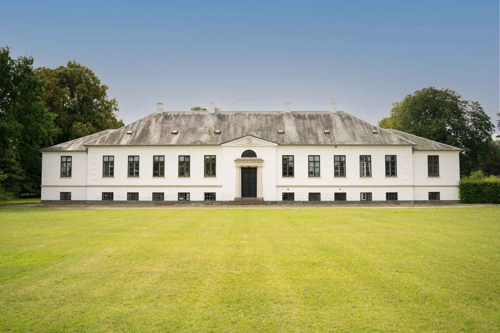 Agerup Gods herregård facade med hvide mure, frontispice og grøn plæne