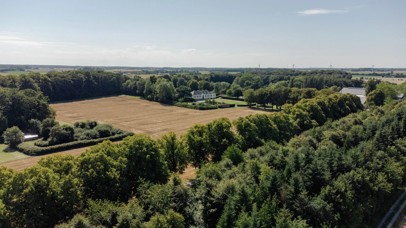 Høstet mark omkranset af skov med herregården på Agerup Gods i baggrunden