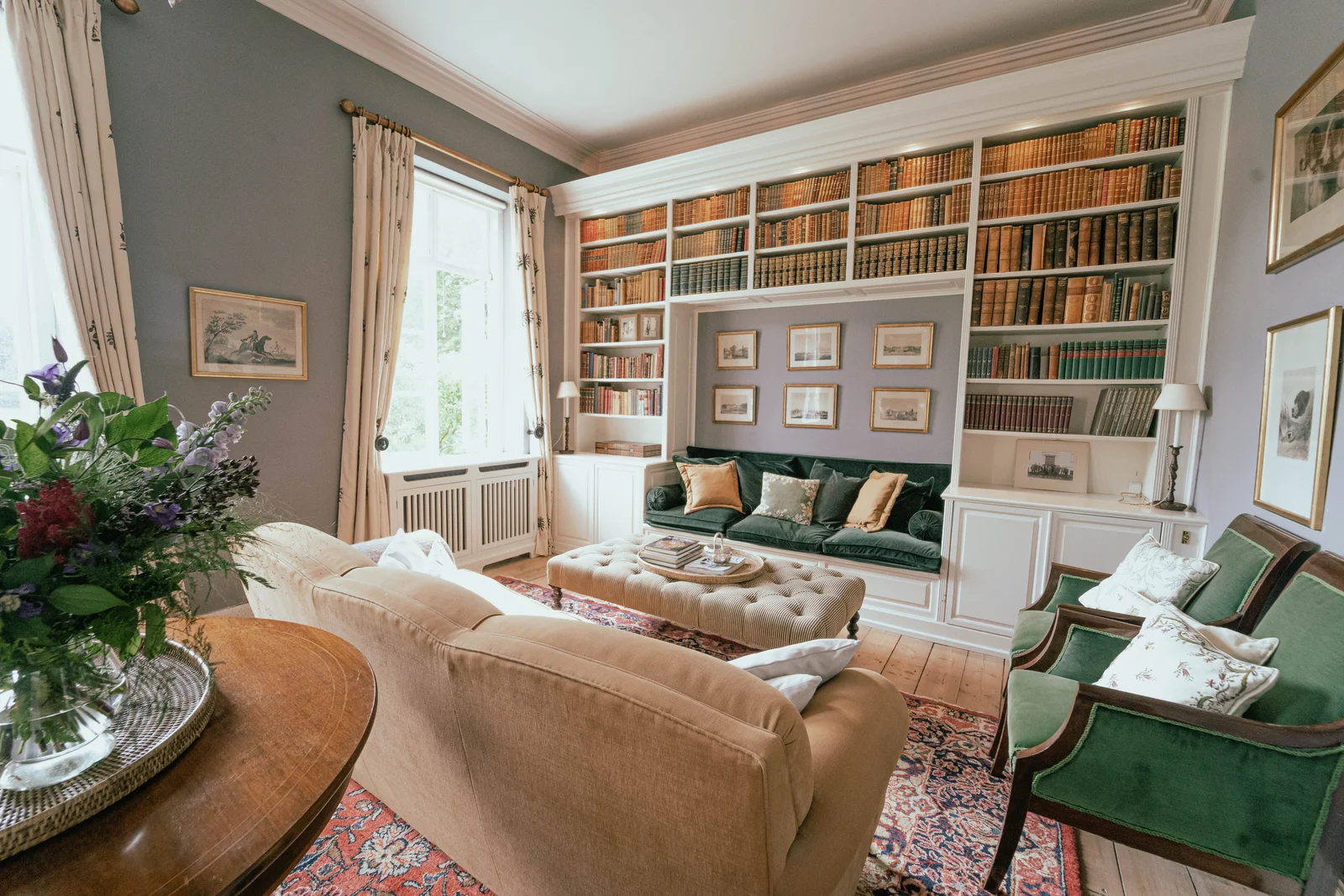 Die Bibliothek von Gut Agerup mit Blumen, Sofa, Hocker und grünen Sesseln