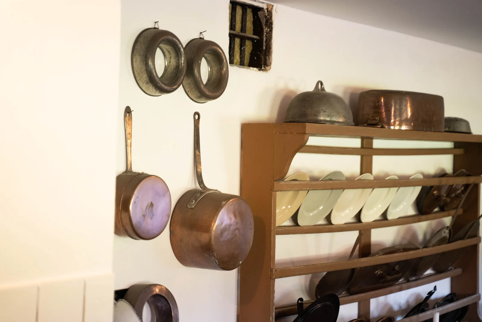 Kupferpfannen und Tellerregal an der Wand der historischen Küche von Gut Agerup