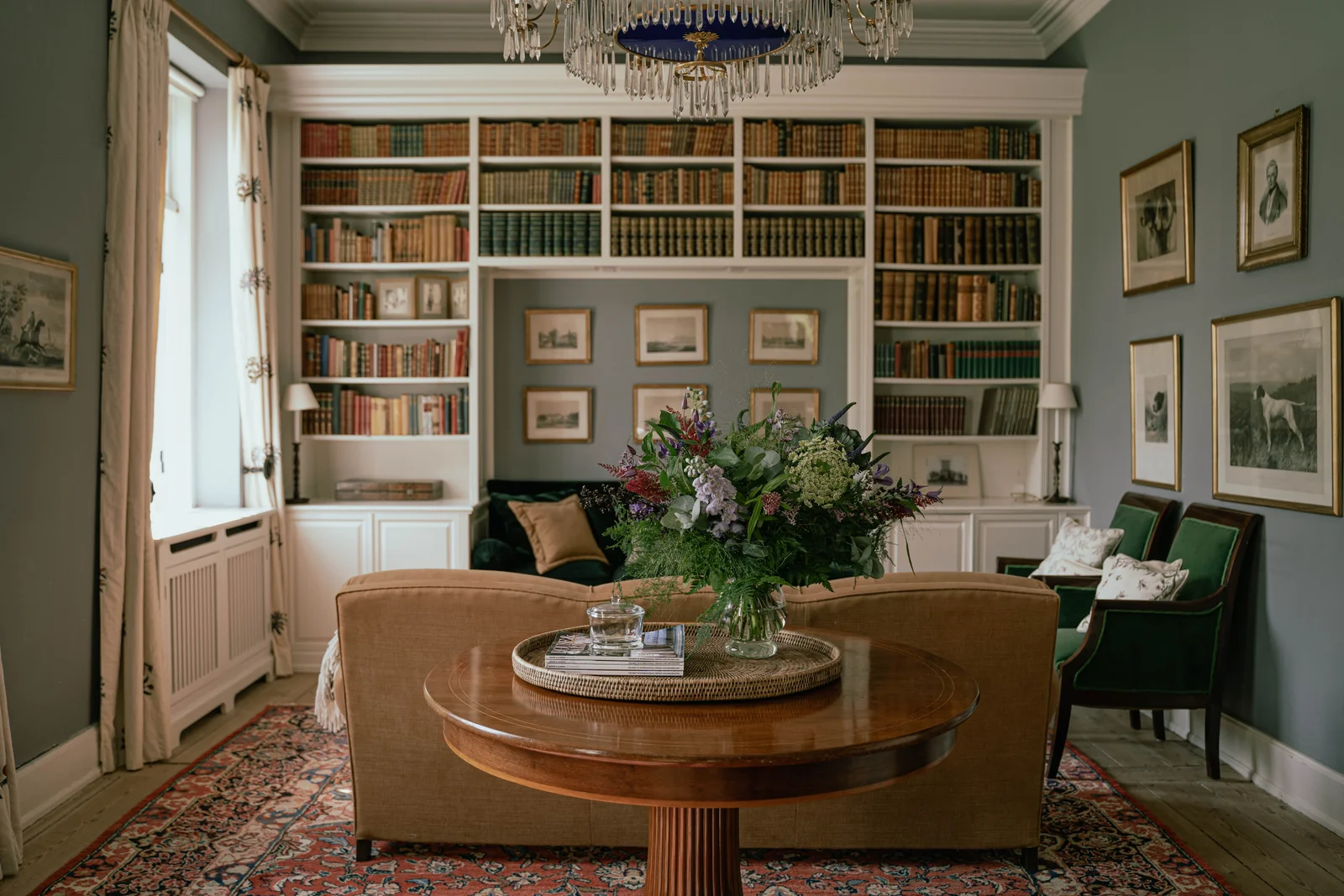 Die Bibliothek von Gut Agerup mit rundem Tisch, Blumenstrauß und Bücherregalen um das Sofa