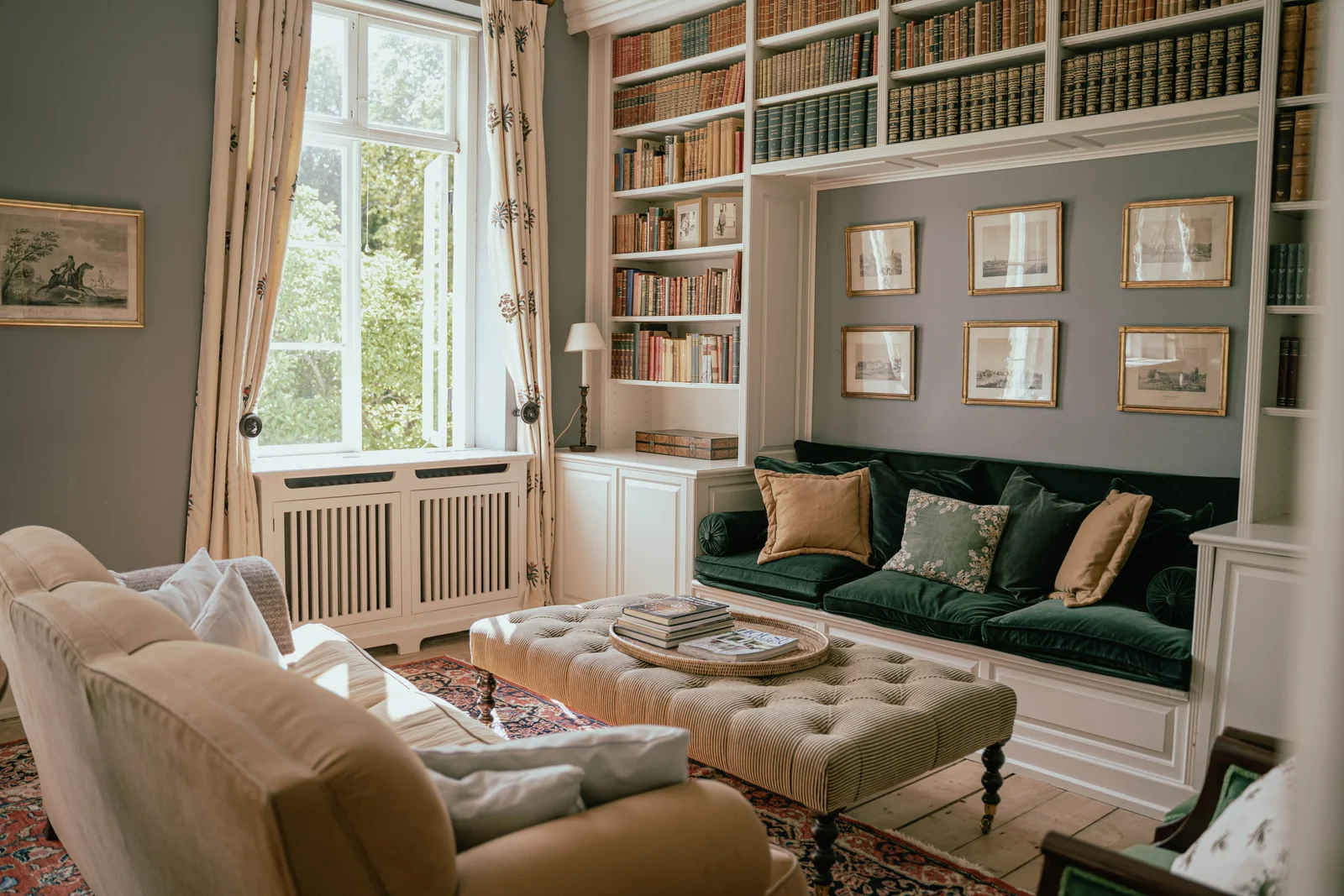 Die Bibliothek von Gut Agerup mit grünem Samtsofa, Hocker und gerahmten Stichen
