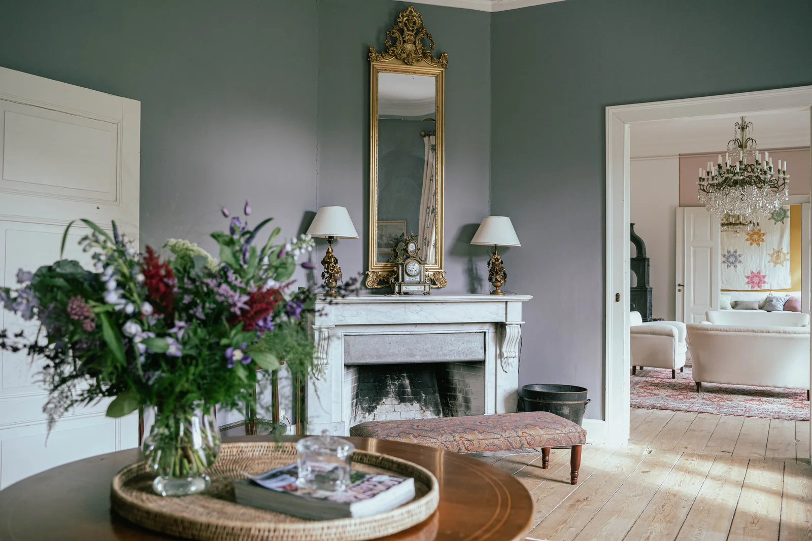 Das Kaminzimmer von Gut Agerup mit Marmorkamin, Blumenstrauß und Blick in den Salon