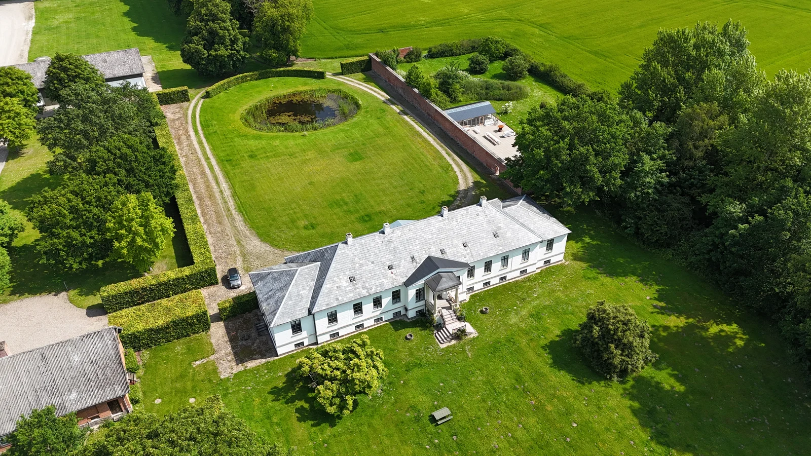 Das Herrenhaus von Gut Agerup und der Rasen mit dem Teich schräg aus der Luft
