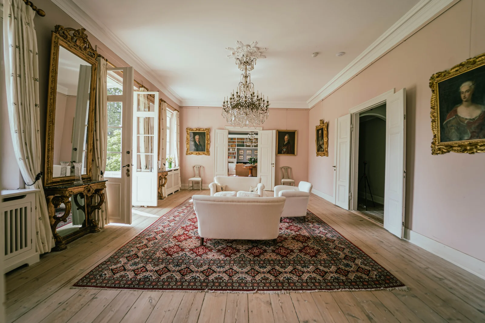 Der Salon von Gut Agerup mit Perserteppich, weißen Sofas und Kronleuchter