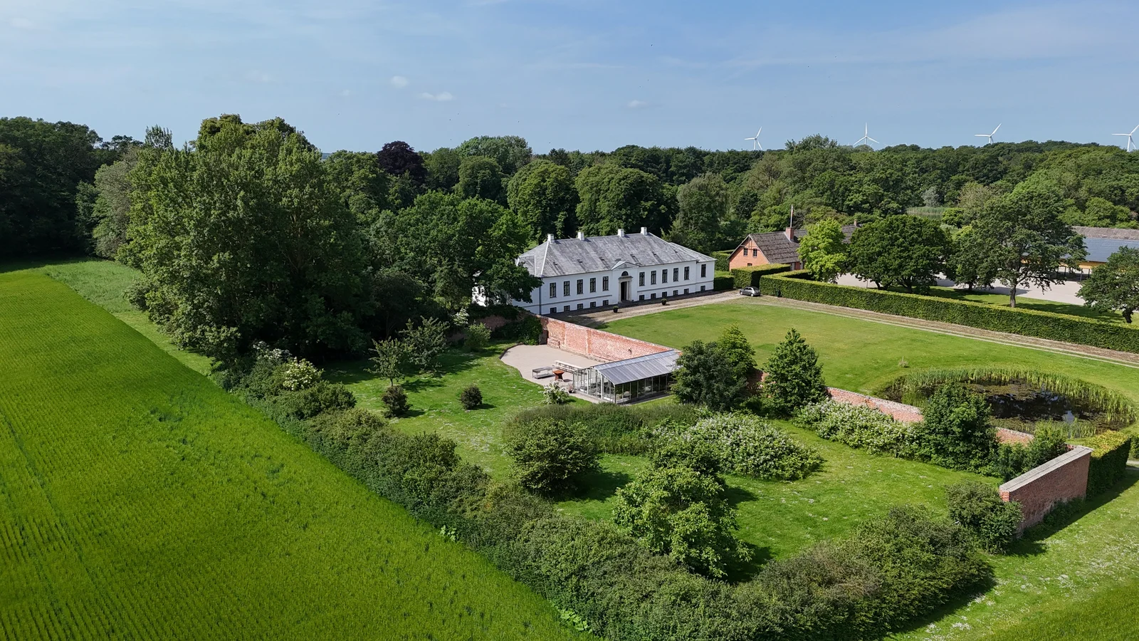 Luftaufnahme des ummauerten Gartens, des Glashauses und des Herrenhauses von Gut Agerup im Sommer