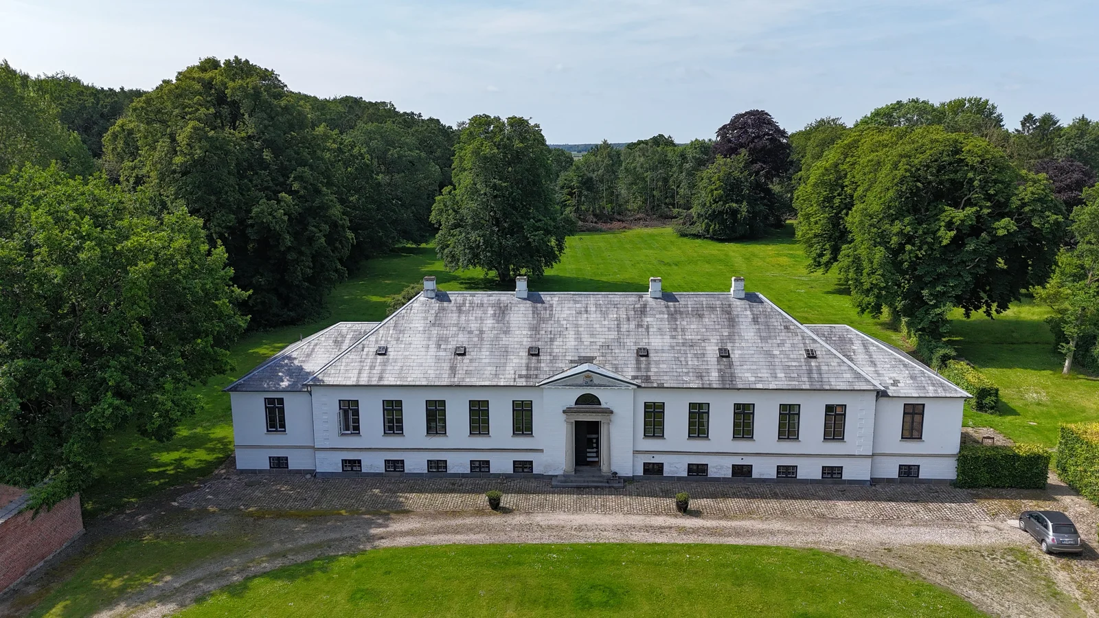 Gut Agerup aus der Luft mit der weißen Fassade des Herrenhauses, dem Vorplatz und dem Rasen